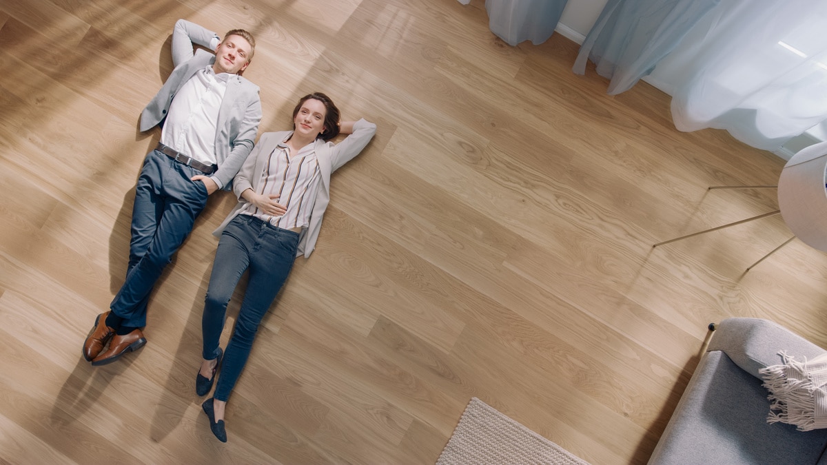 young couple are lying on a wooden flooring in an apartment. the